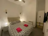 Double bed in the interior apartment with lit wall lamps above the headboard and a remote control on the nightstand